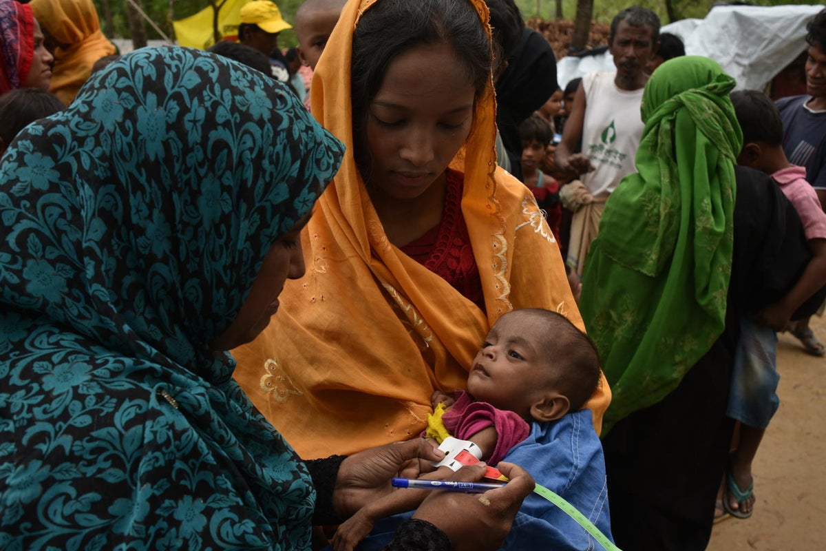 A woman is holding her baby while a health worker assesses them for malnutrition.