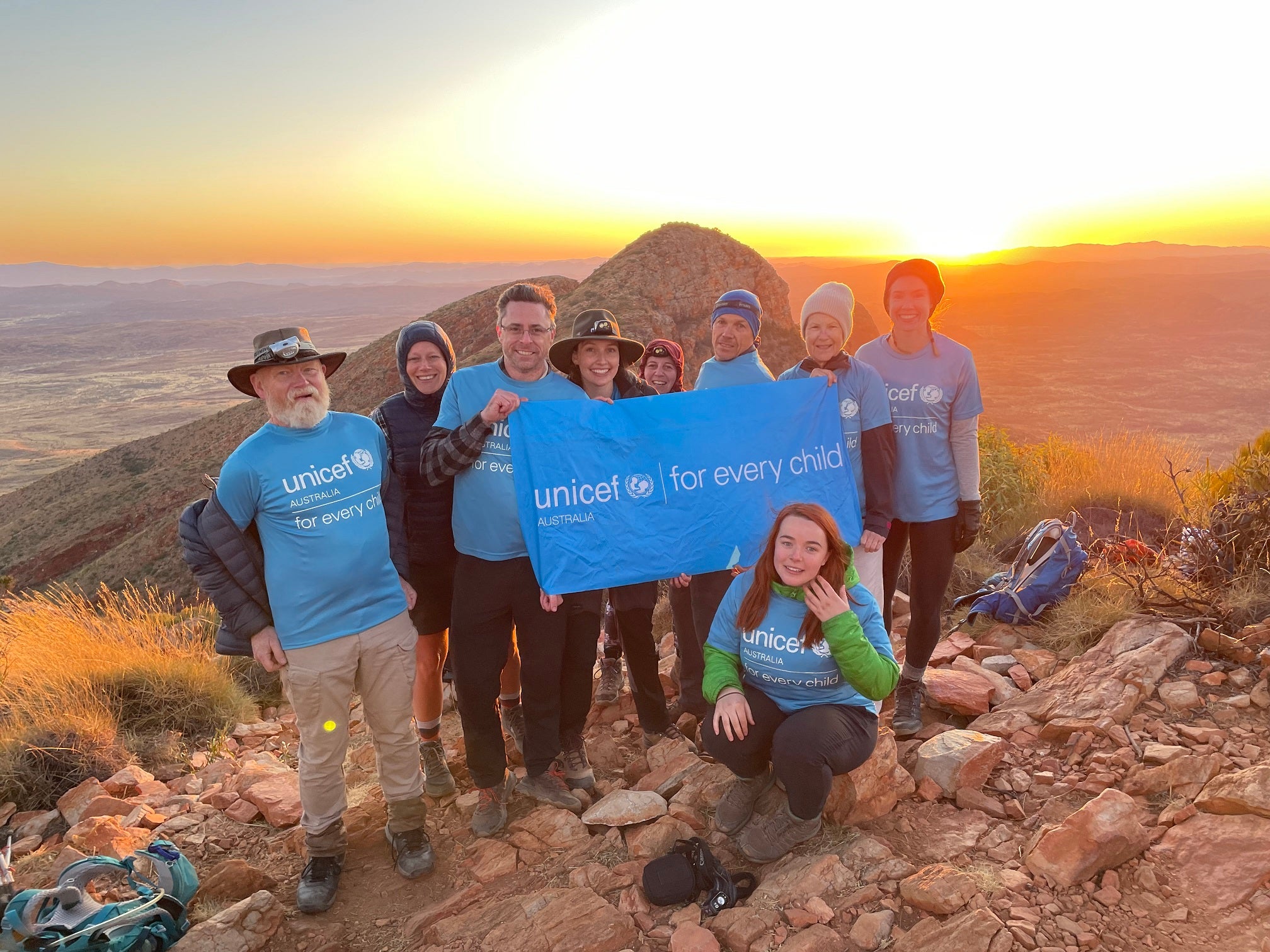 A group of people wearing UNICEF t-shirts. They are on top of a hill and the sun is rising behind them.
