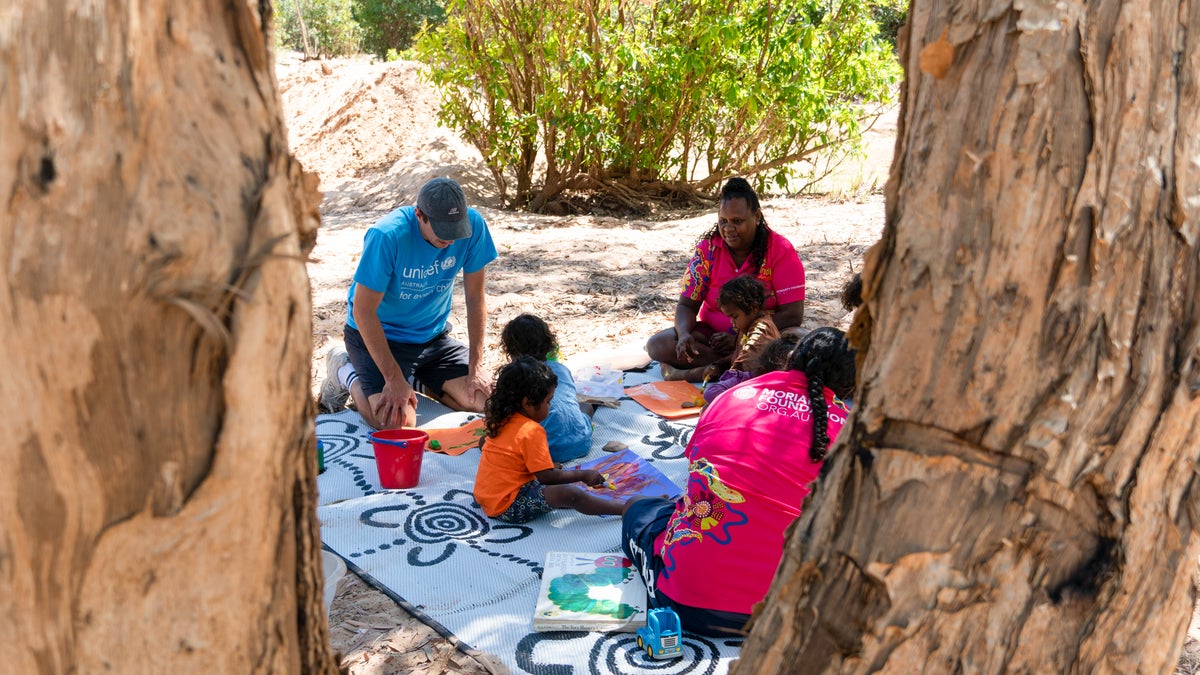 A group of adults and children sitting on the ground reading books.