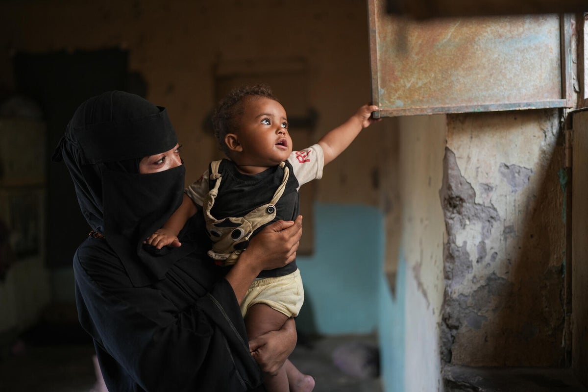 A two-year old is held by his mother inside their home, healthy after recovering from malnutrition.