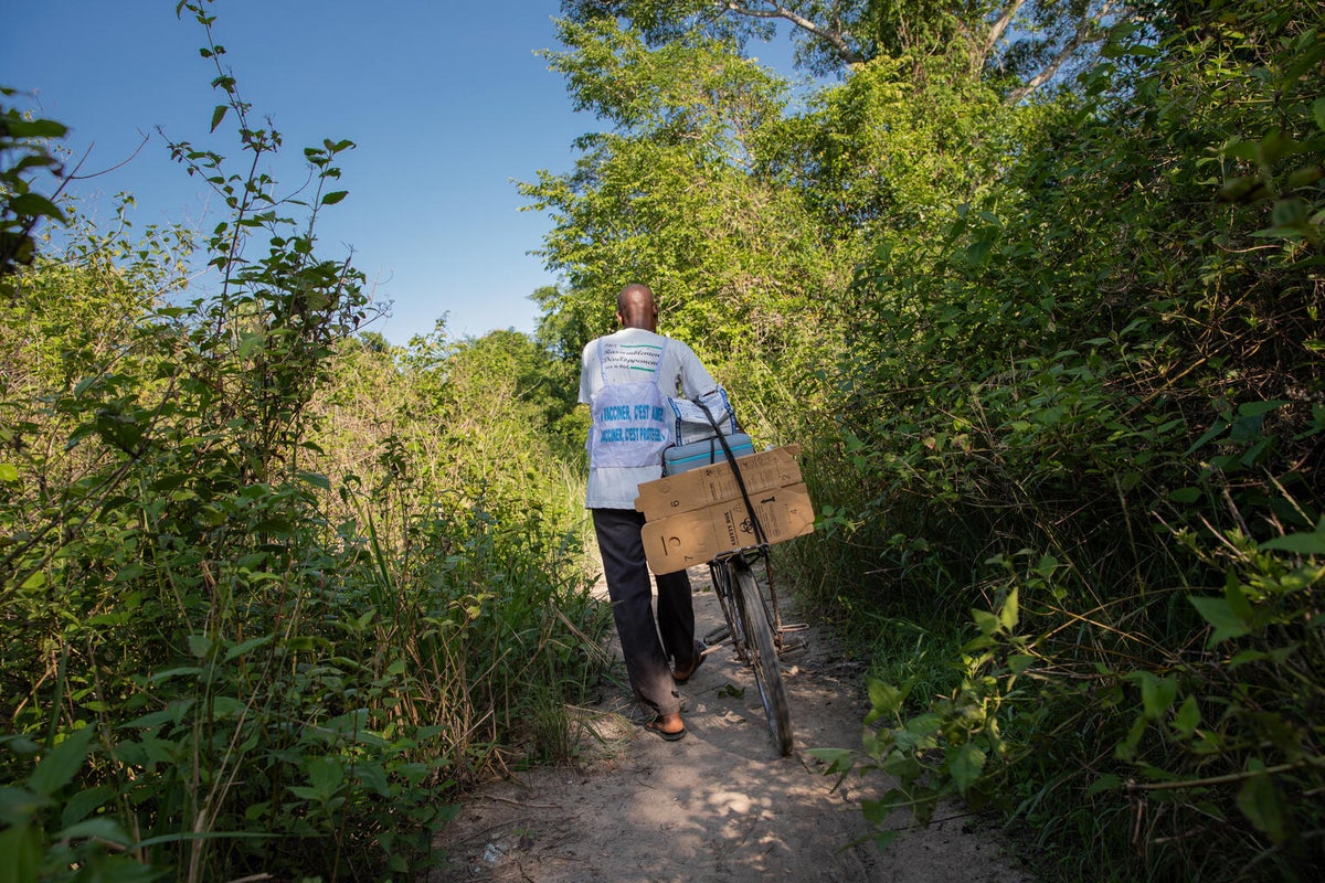  
A man pushing his bicycle through dirt road with vaccine carriers.