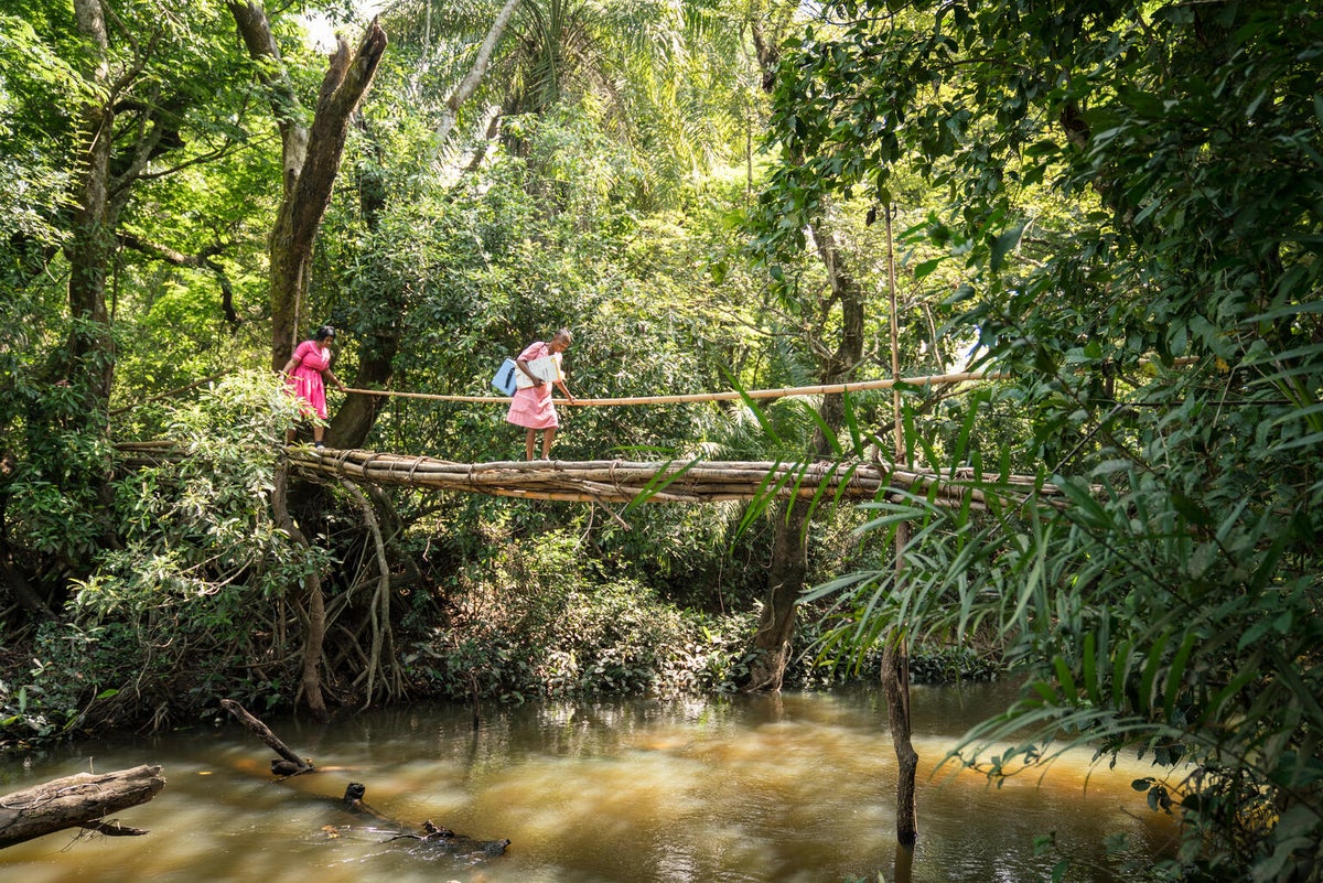 Two nurses cross a small bridge carrying medical supplies.