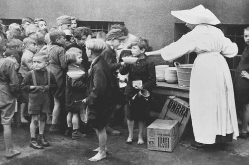 In Poland, 1946, a nun serves bowls of soup to a group of children who get their only meal for the day at this UNRRA-supplied kitchen in the Slask Dabrowski district. UNRRA (later UNICEF) boxes are by her feet. © UNICEF/UNI43101/Kubicki