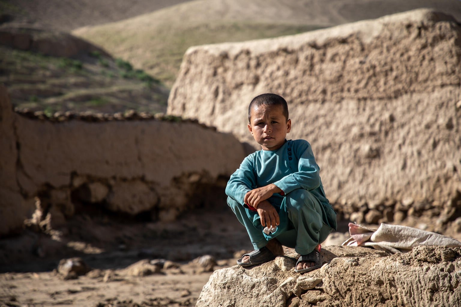 A young boy in Afghanistan sits outside his destroyed home.