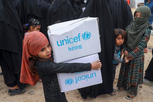 A young girl is carrying two boxes with the UNICEF logo on them.