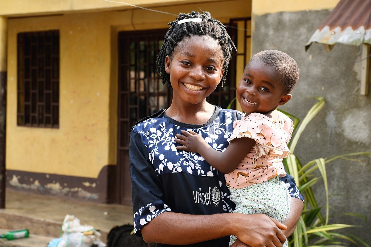 A young woman with a toddler on her arms. They are both smiling.
