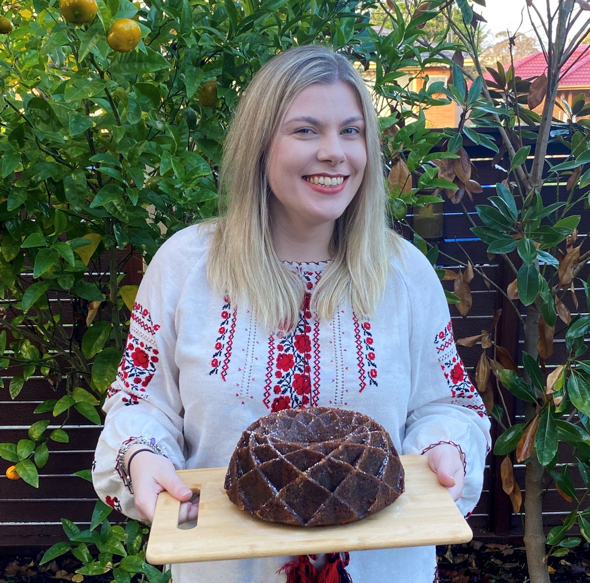 Nicole Campbell, wearing a traditional vyshyvanka, is holding the Ukrainian Honey and Poppyseed cake which was baked while fundraising for #CookForUkraine.