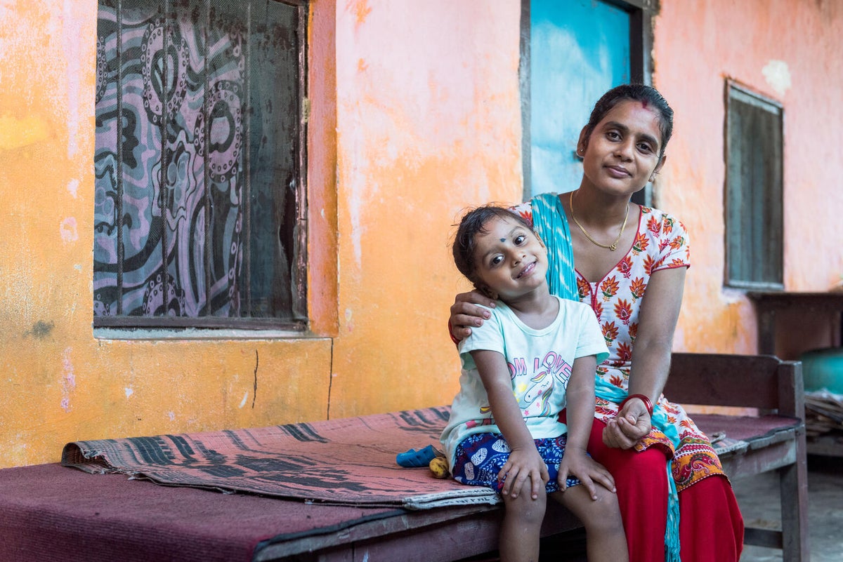 A young girls seating next to her mum. Both of them are smiling to the camera.