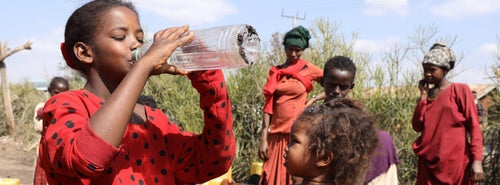 A young girl drinking water from a bottle in her village. 