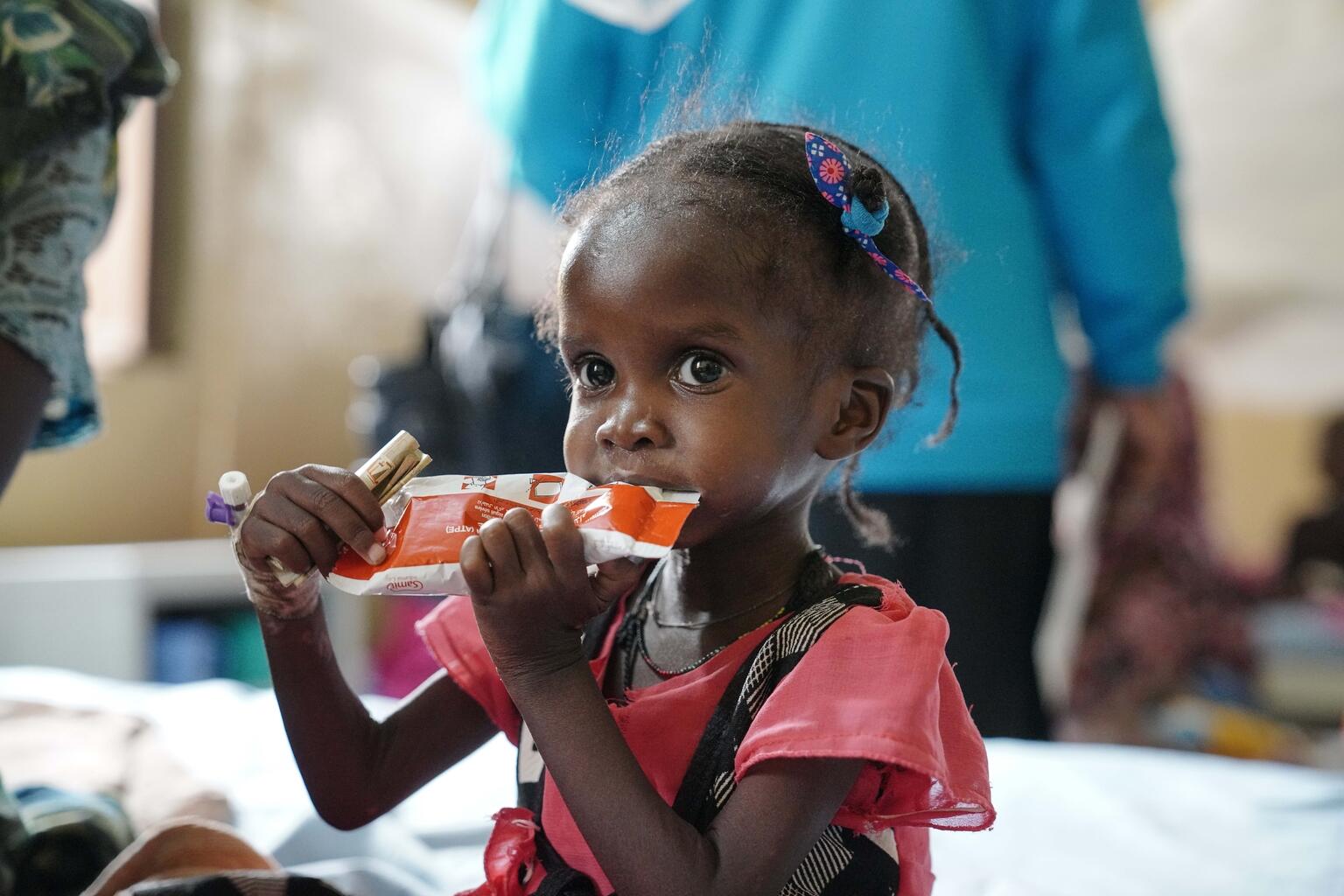 A Sudanese child suffering from malnutrition sits and eats a plumpy nut, a type of ready-to-use therapeutic food. 