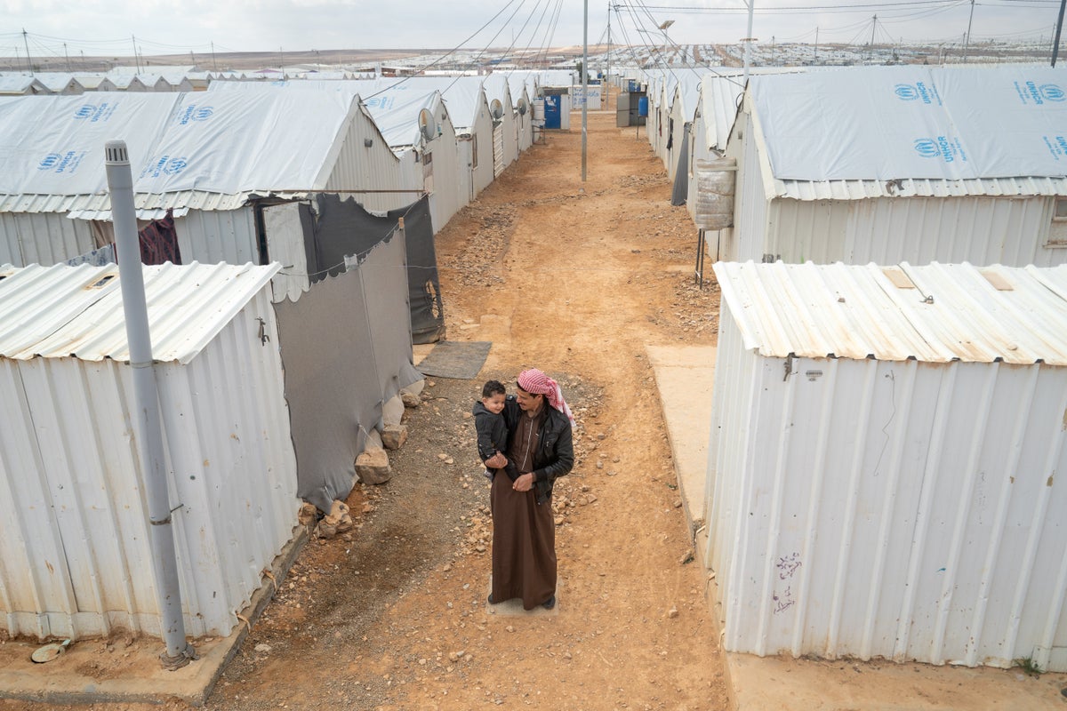 Father holds his baby boy outside refugee camp.