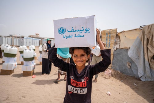 At a camp in Yemen, a young boy carries a box of supplies back to his family's tent. 