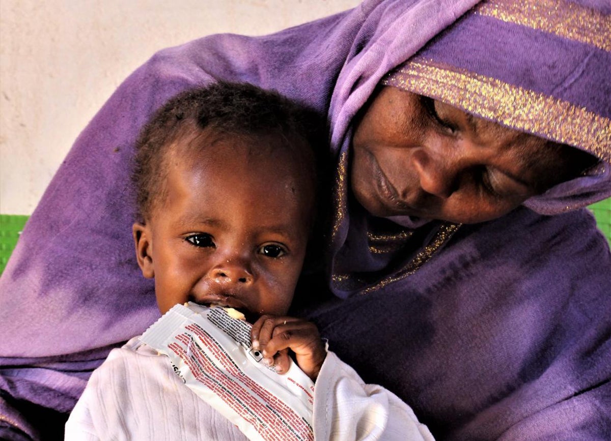 Mother holds baby who is crying, eating therapeutic food