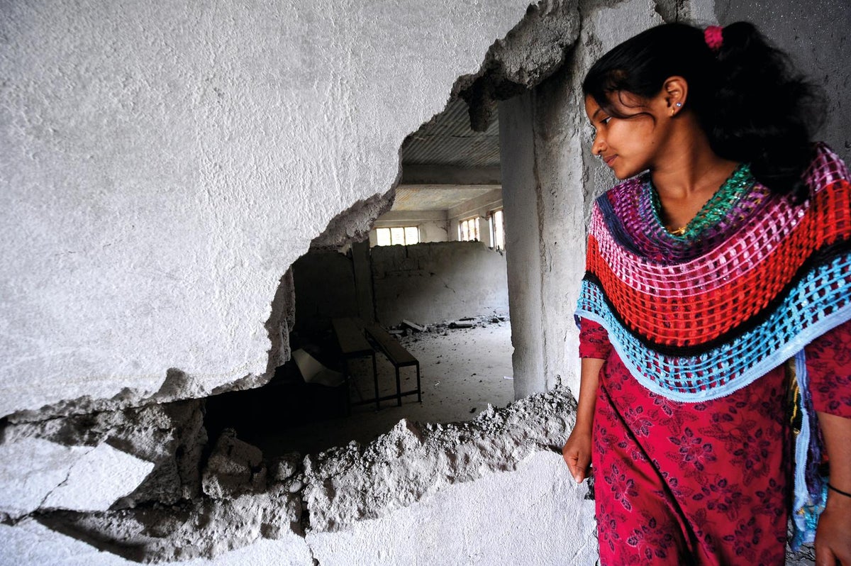 A girls is standing next to a wall that has a large hole.