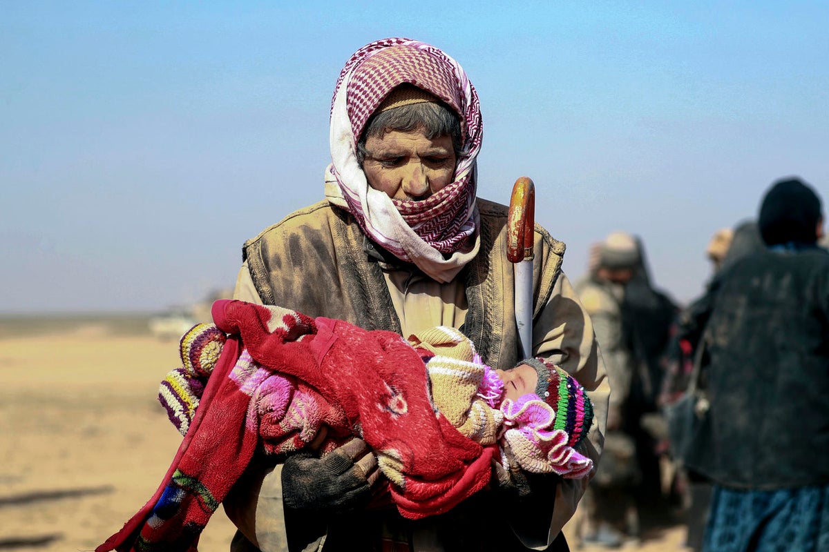 A man carries a child through the desert, Syria