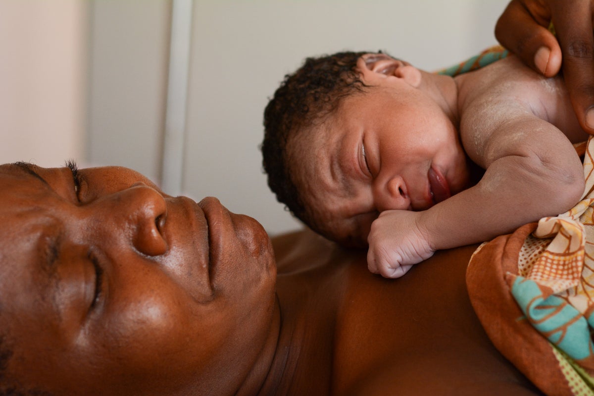 A woman is lying down and has a newborn baby on her chest.