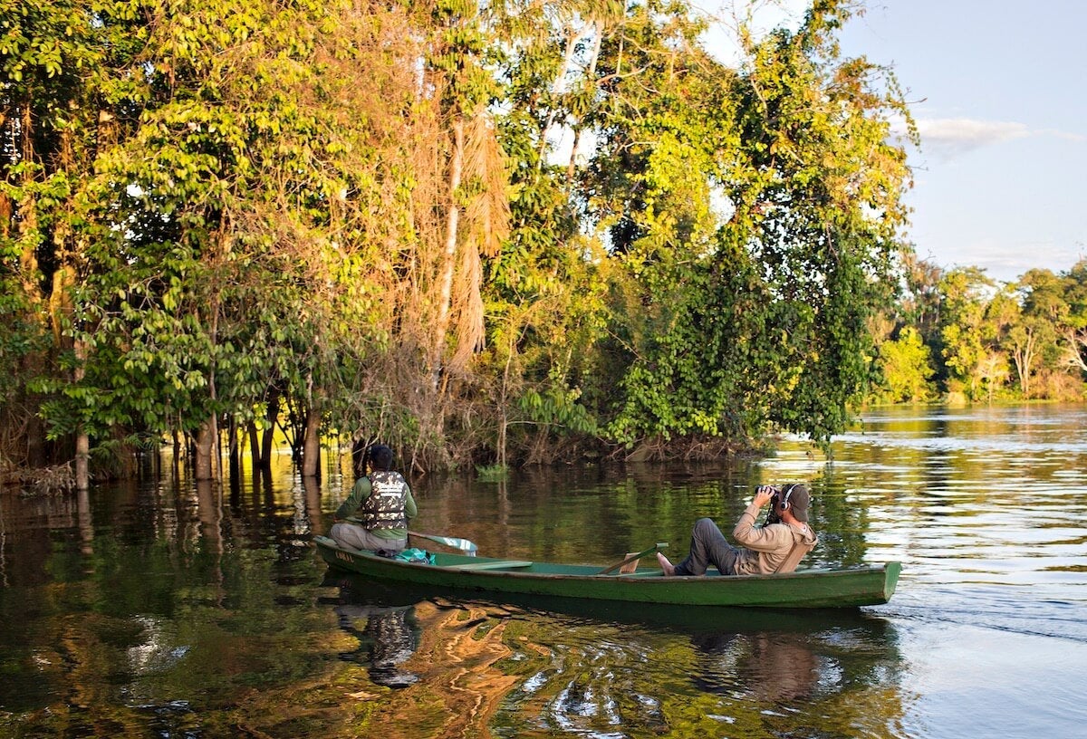 Two people in a green canoe on a river in the rainforest