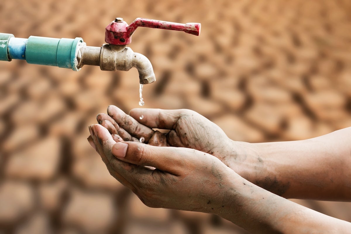 Dirty hands cupped underneath a dripping faucet