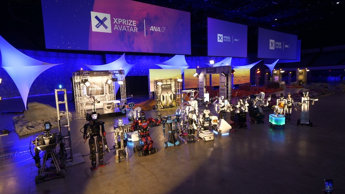 Robots on a stage in front of signs with the ANA Avatar XPRIZE logo