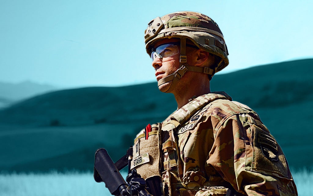 profile shot of man in military uniform in the field, mountains in the background
