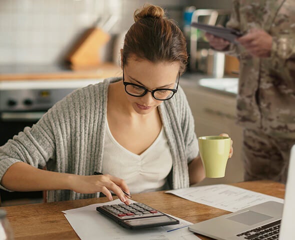 A young military spouse with glasses managing her finances while using a calculator and reviewing paperwork.