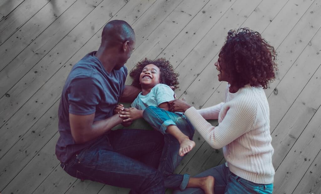 Image of two parents playfully tickling their child on the floor.