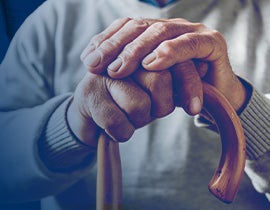 Close-up of an older adult’s hands resting on a wooden cane.
