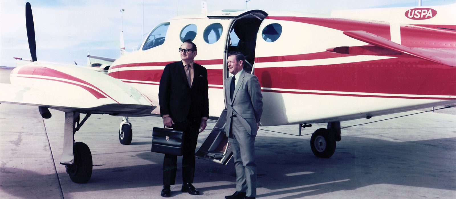 Two men standing in front of a small plane on a runway