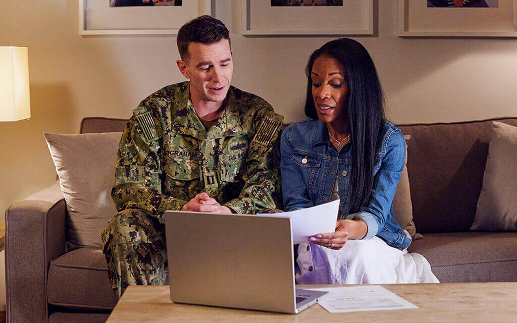 Image of a man in uniform and a woman sitting and discussing a budget on a couch.
