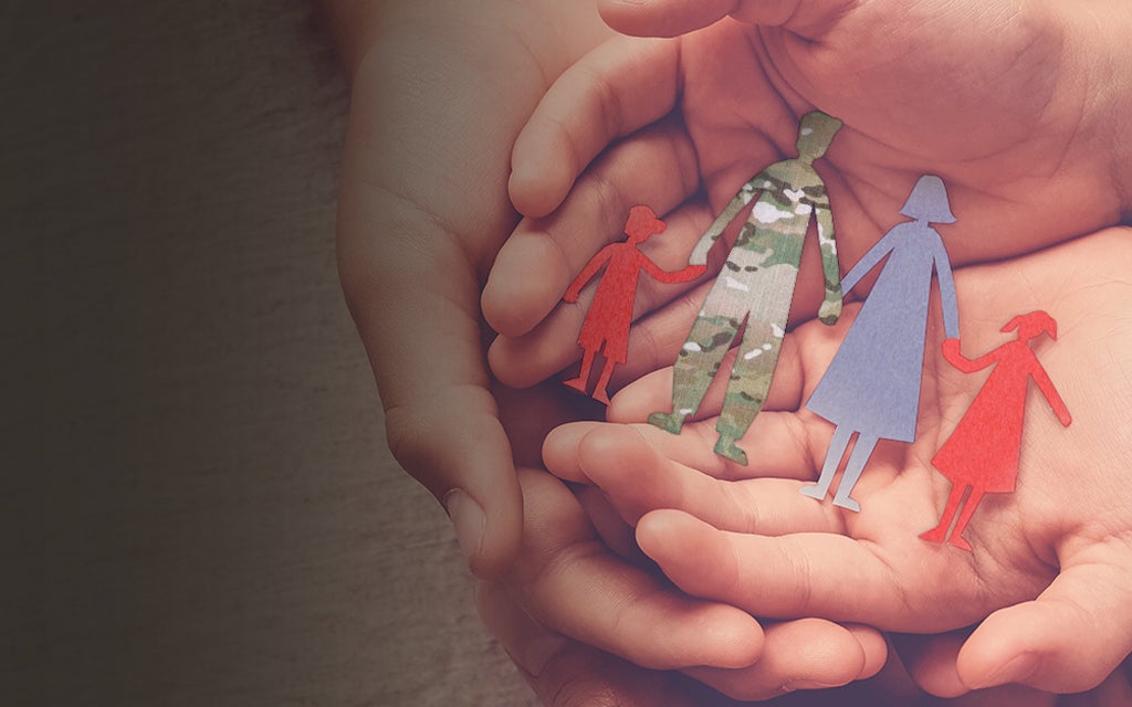 A hand holding cut out shapes of a military family.