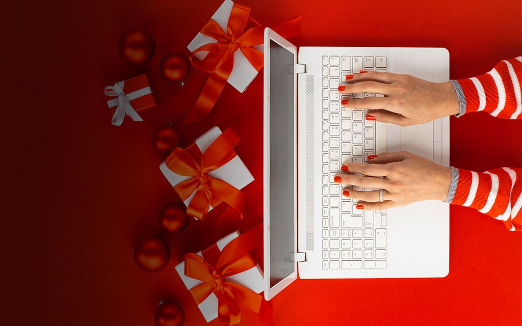 An image of a person typing on a computer with red and white holiday gifts around.