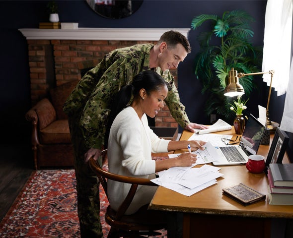 Military family members review financial paperwork and plan goals together at a home workspace.