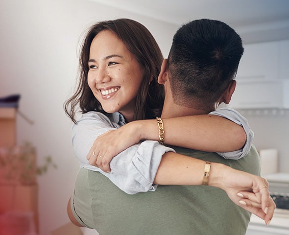 A person is lifted into an embrace, arms wrapped around another individual in a warm, welcoming hug inside a bright, modern home.