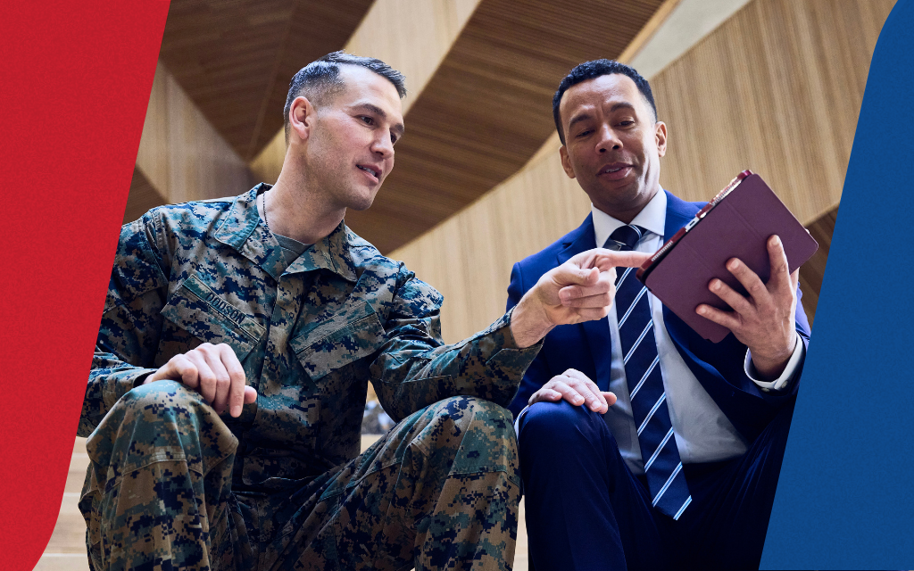 man in a service uniform sitting next to another man in a suit, both looking at something on a tablet