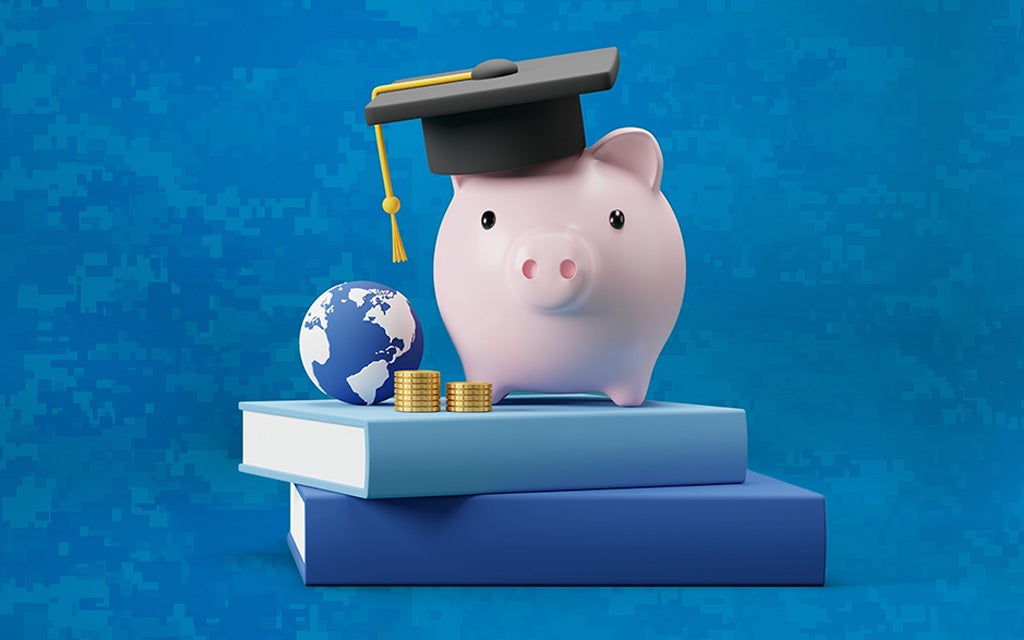 a pig wearing a graduation cap, perched atop 2 books, next to a stack of coins and a globe