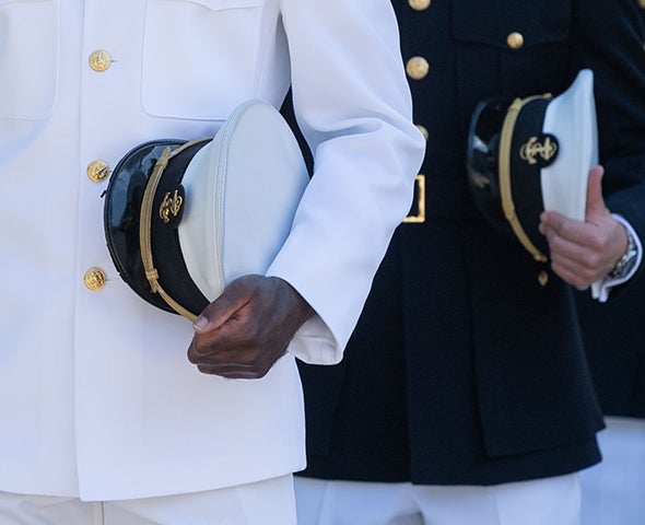 Image of two military members in the navy standing holding their hats.