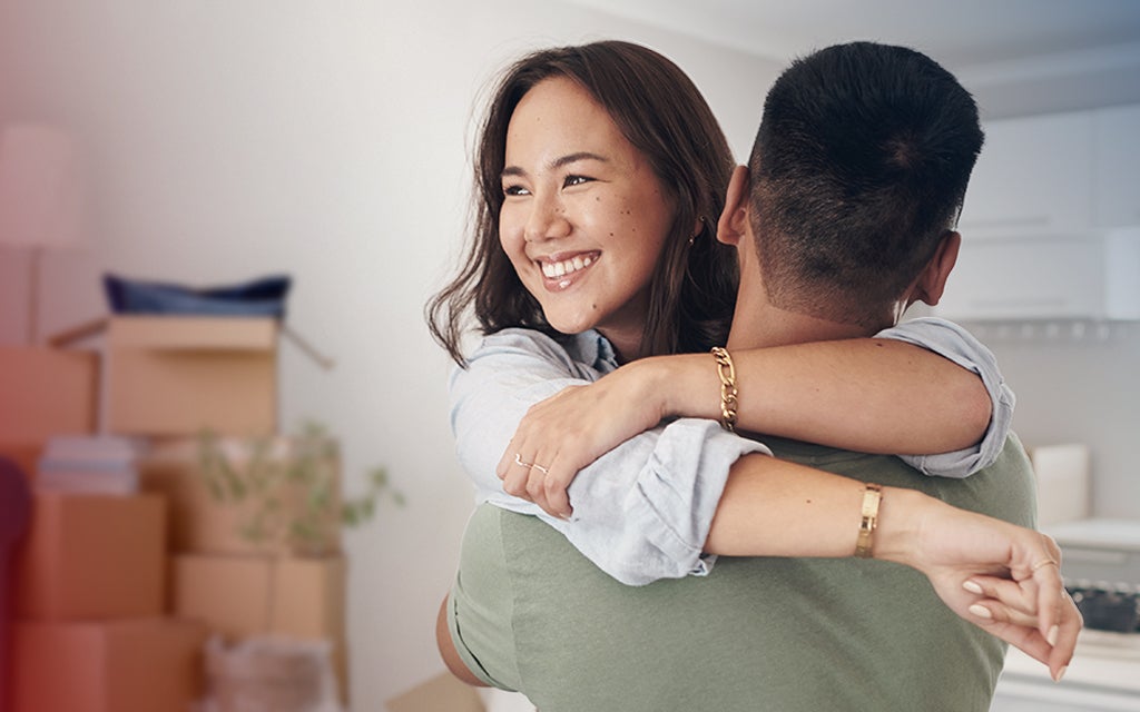 A person is lifted into an embrace, arms wrapped around another individual in a warm, welcoming hug inside a bright, modern home.