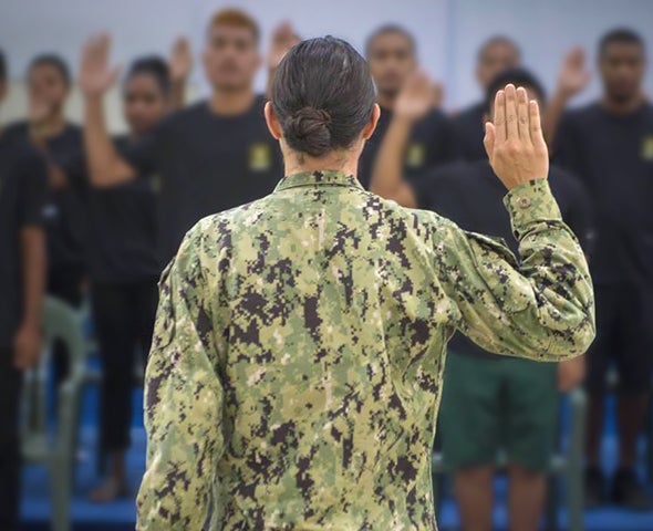 Soldier standing facing away with right hand raised in oath.