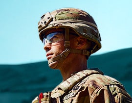 profile shot of man in military uniform in the field, mountains in the background
