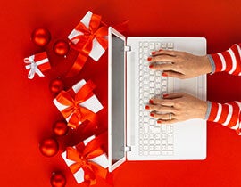 An image of a person typing on a computer with red and white holiday gifts around.
