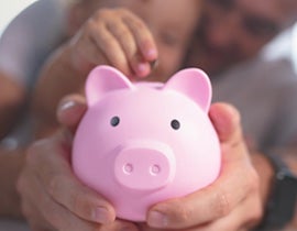 Father and child putting cents into a pink piggy bank.