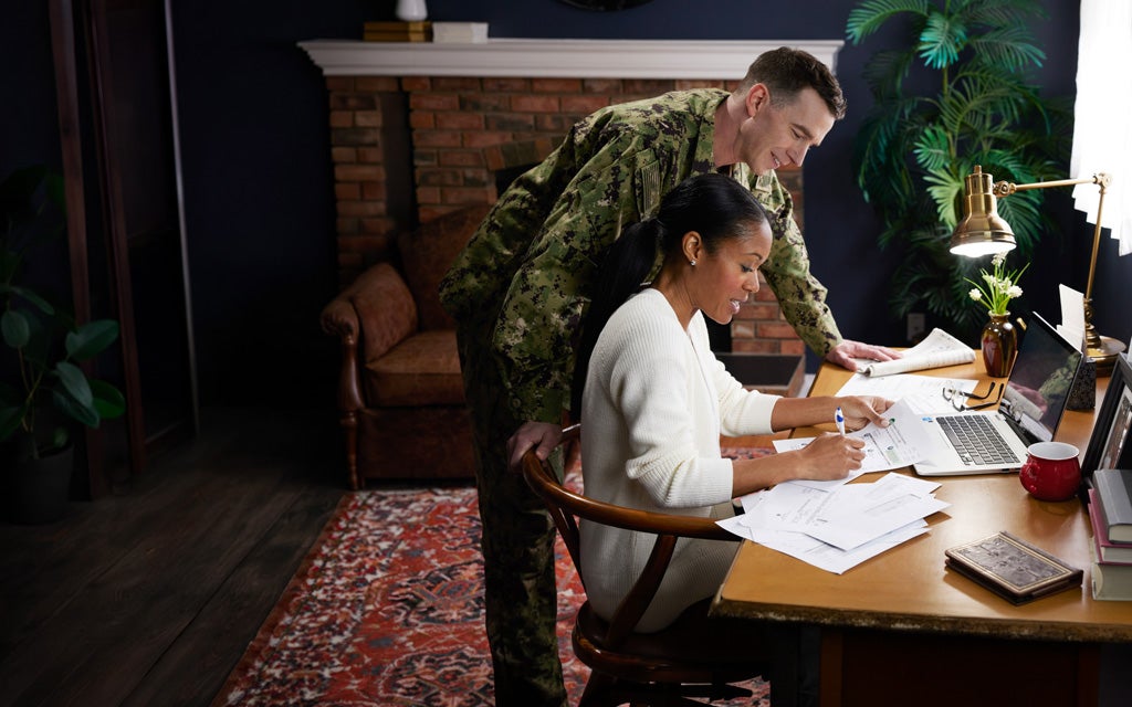 Military family members review financial paperwork and plan goals together at a home workspace.