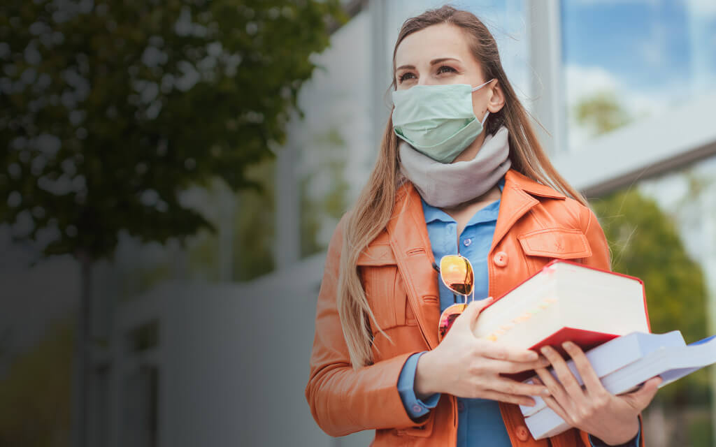 Female college student carrying books wearing a face mask during pandemic.