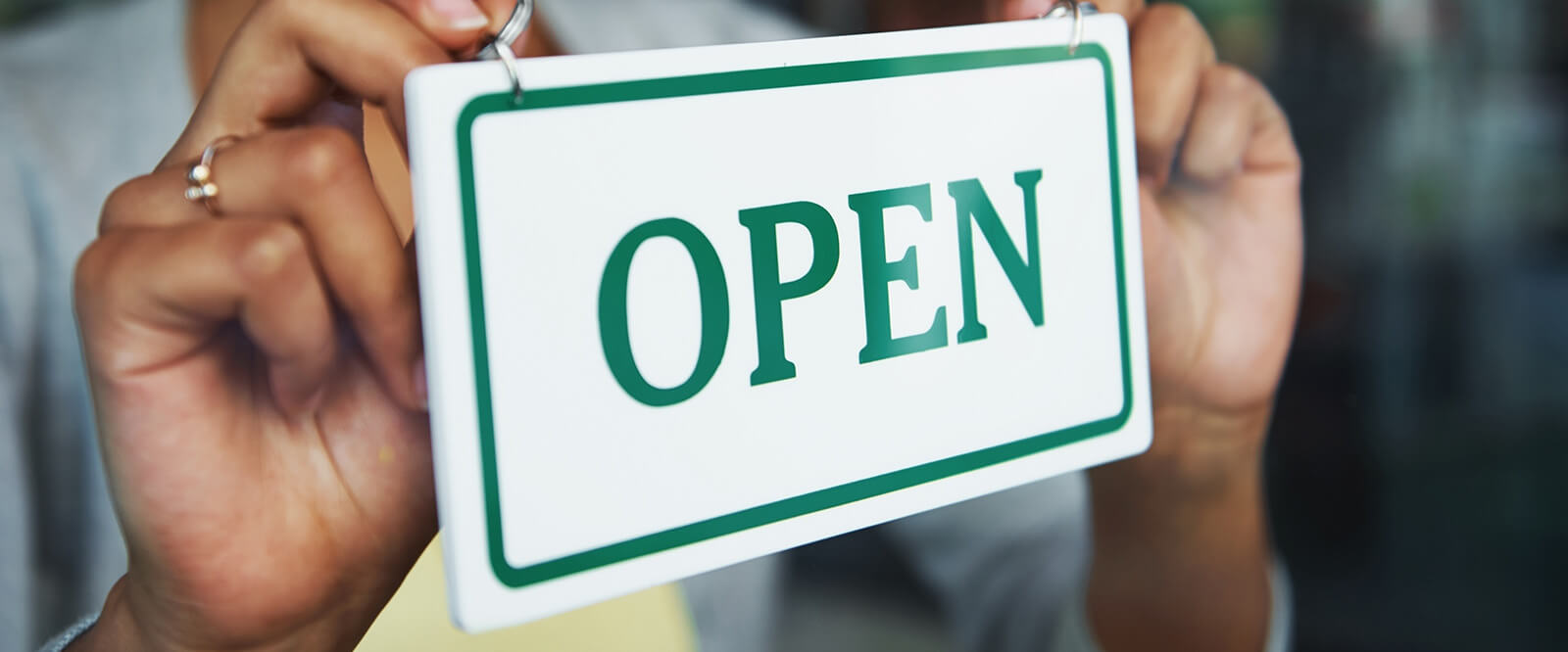 Image of a person holding an open sign against the glass of a window pane.