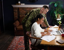 Military family members review financial paperwork and plan goals together at a home workspace.