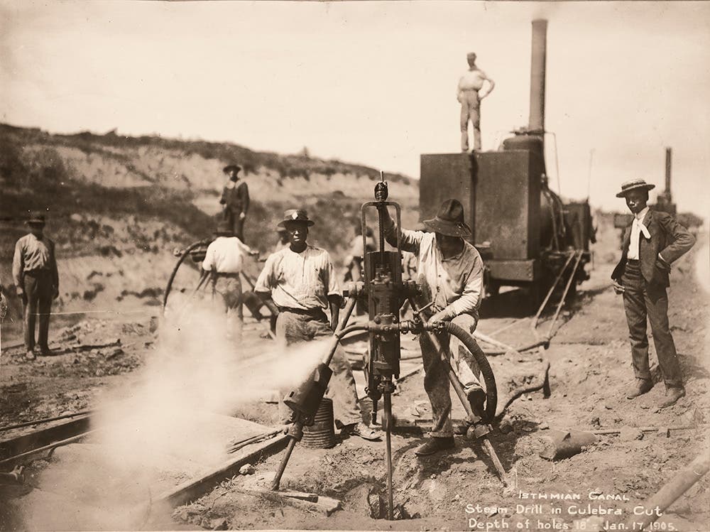 A salvaged French tri-pod steam drill in Culebra Cut, January 1905.
Holes 18 feet deep were drilled into rock. After drilling, the holes were “sprung” by lowering four to six sticks of dynamite and igniting them to create a small chamber into which 25 to 200 pounds of explosive were tamped to blast out the rock. View in Digital Collection »