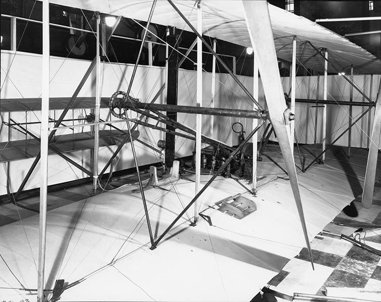 Engine built by Charlie Taylor in place on the wing of the Flyer; the pilot (Wilbur or Orville) would lie on the cradle next to the engine, balancing its weight (airandspace.si.edu)