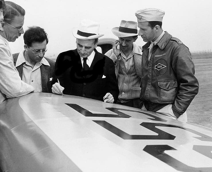 Theodore von Kármán making notes on the wing of the Encoupe aircraft that is about to take off with rocket assist; Jack Parsons, who was not a Caltech student, has been cropped out of the photo at the left by the JPL publicity team. Frank Malina is between von Kármán and the pilot (Wikimedia commons)