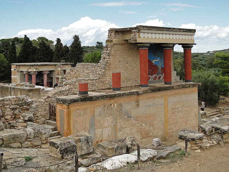 View of the North Portico, Knossos, with a bull fresco protected by a ceiling added by Evans; columns and concrete wall were added by Evans as well (Photo by Bernard Gagnon via Wikimedia commons)
