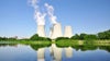 Cooling towers of a nuclear power plant releasing steam on a sunny day with greenery in the foreground